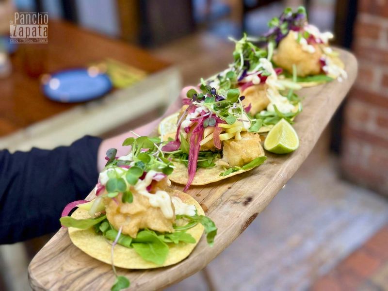 Primer plano de tacos de pescado capeado estilo Baja con col y salsas tradicionales.