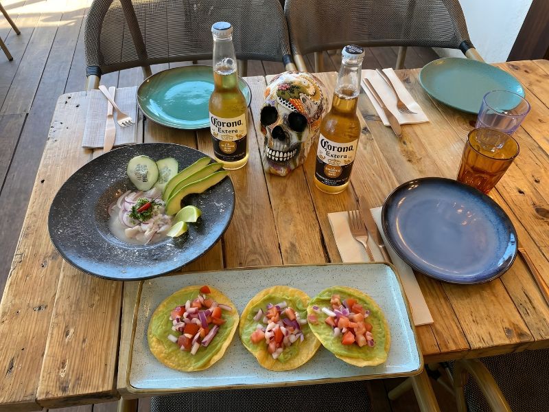 Primer plano de tacos al pastor y margaritas sobre una mesa con mariachis tocando al fondo en De Pancho a Zapata.