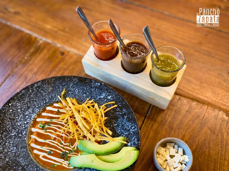 Primer plano de un taco al pastor recibiendo unas gotas de salsa picante artesanal en Pancho.