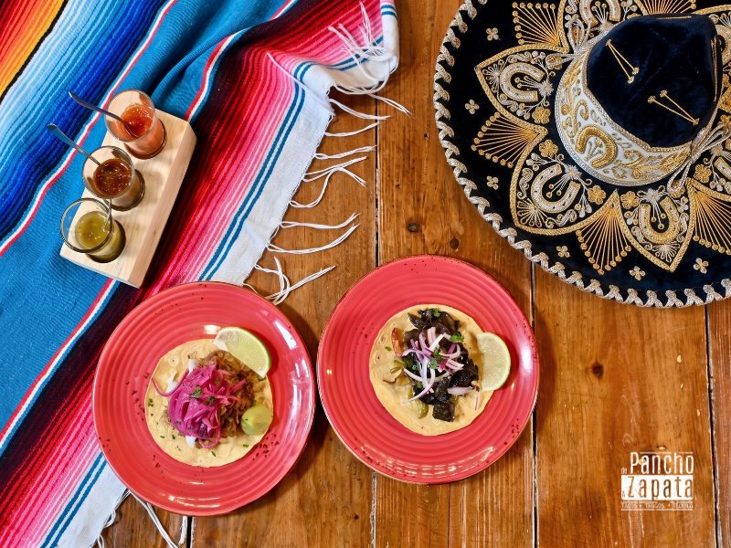 Tacos al pastor y micheladas heladas servidas en Pancho con ambiente de fiesta mexicana de fondo.