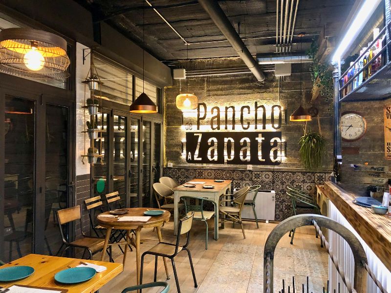 Interior de De Pancho a Zapata en Torrelodones, con mesas preparadas y el rótulo del restaurante iluminado