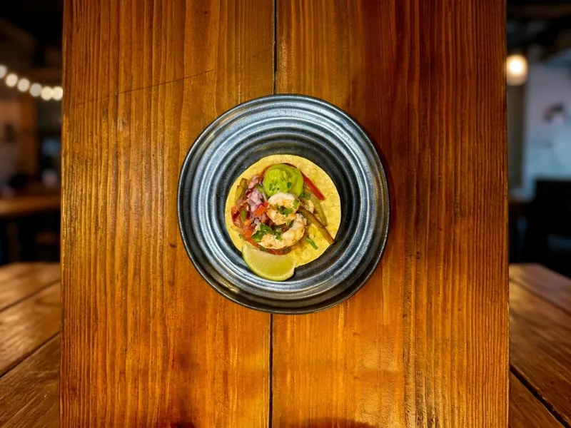 Taco del gobernador con camarones, pimiento, cebolla morada, crema de aguacate y lima